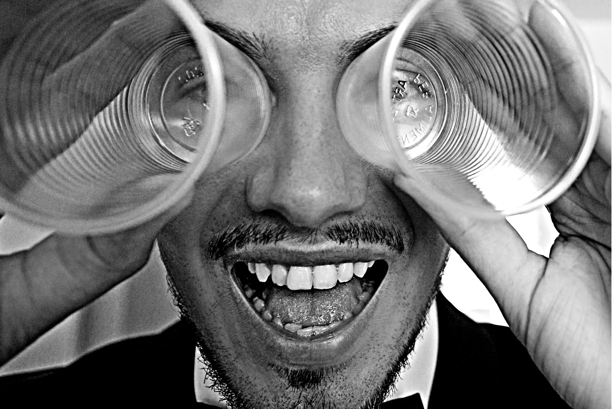 Ritratto ironico dello sposo in bianco e nero con bicchieri di plastica sugli occhi, fotografia di matrimonio spontanea a Napoli.